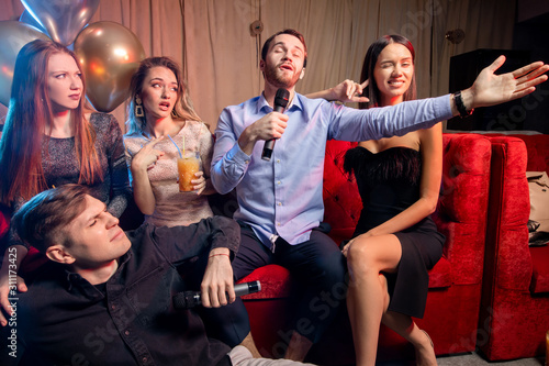 cheerful young caucasian people have positive mood while spending time in karaoke bar, attractive ladies and handsome guys celebrating, have party indoors, in karaoke bar