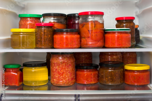 Canned vegetables and jams on refrigerator shelves.