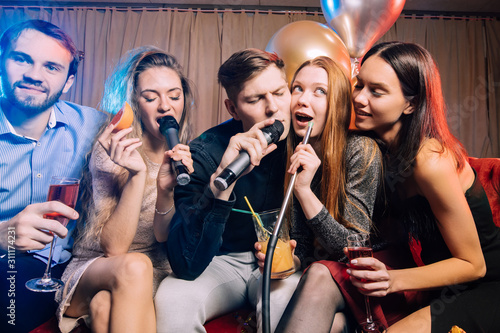 Fotografie group of happy young friends of caucasian appearance having fun in karaoke bar,