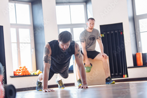Two friends of men athletes doing strength training and interval workout in the gym. Concept of a healthy lifestyle and trend for sports