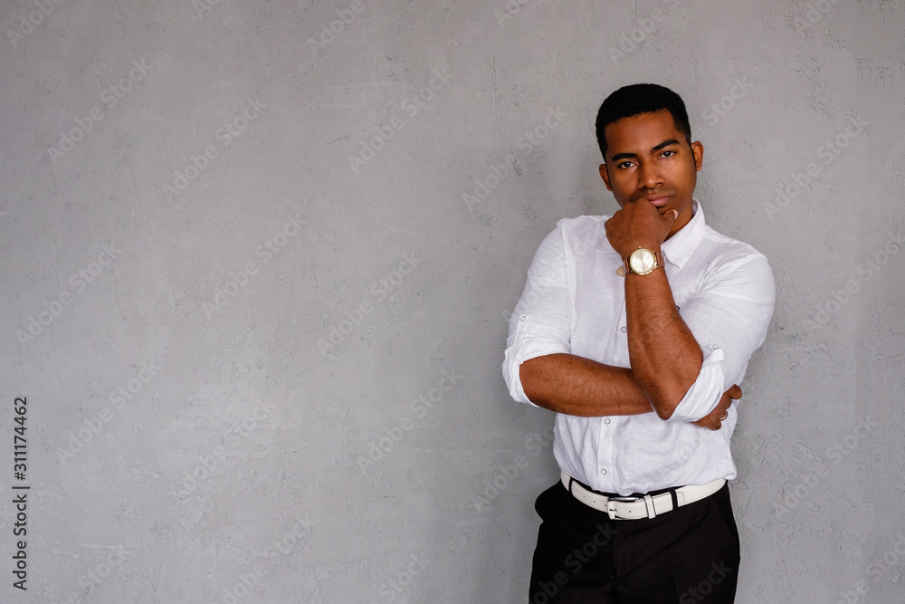 A young pensive man stands against a gray concrete wall. An entrepreneurial man is thinking about a future project. Male African director of an advertising agency. Difficulty concept A young pensive man stands against a gray concrete wall. An entrepreneurial man is thinking about a future project. Male African director of an advertising agency. Difficulty concept