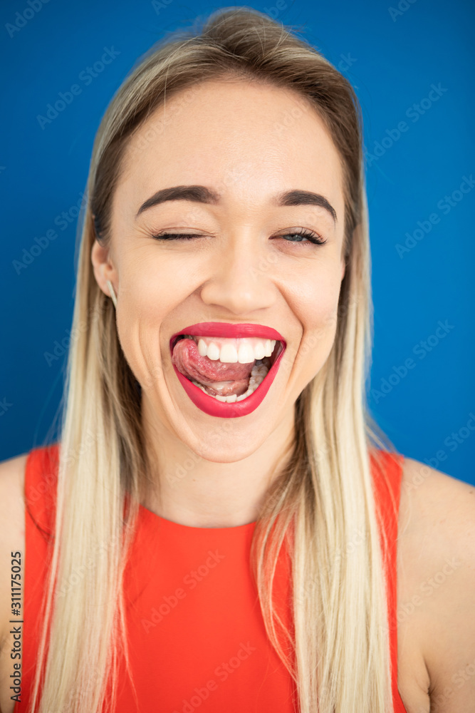 Flirting playful blonde woman portrait. Tongue out. Red lips blue background Flirting playful blonde woman portrait. Tongue out. Red lips blue background