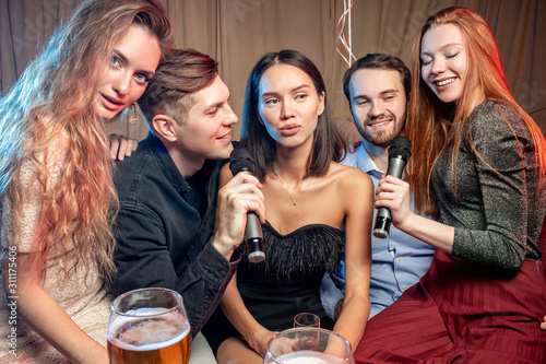 group of young caucasian people in party clothes have free time. leisure time in karaoke bar, enjoy singing, drinking