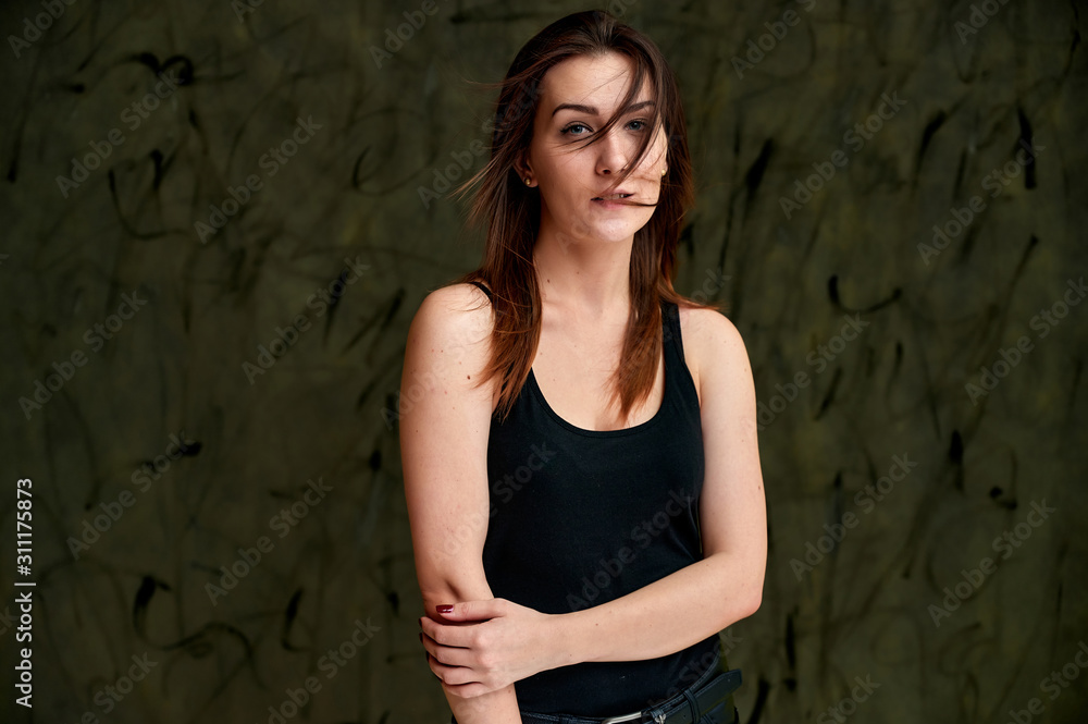 Beauty concept, stylish portrait. Photo of a pretty glamorous brunette girl in a black t-shirt with flying hair on a gray fashionable original background.