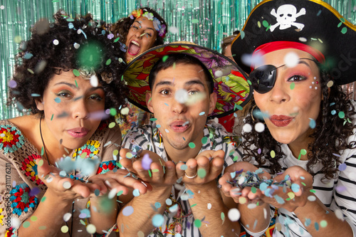Dressed brazilian Friends making party in the night. People blowing confetti. Three people look at the camera with their hands in front. Carnival in Brazil