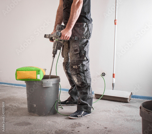 Bauarbeiter rührt Ausgleichsmasse an, spachtelt den Fußboden und bereitet so den Boden für das Parkettlegen vor photo