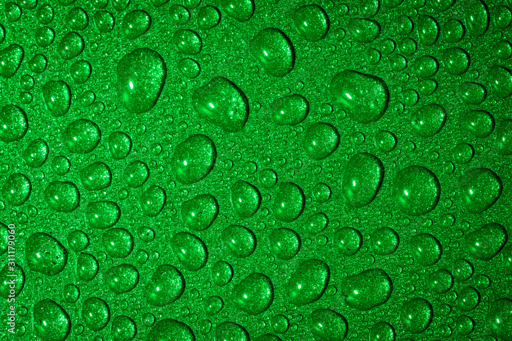 A close up abstract macro photo of water droplets on a grey non stick frying pan material lit with a green flash gel