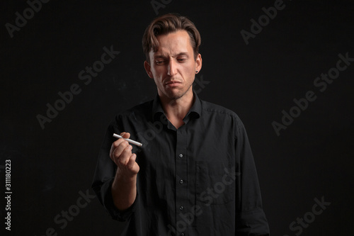 Young man looking with disgust at the cigarette over black background. Time to leave off smoking.