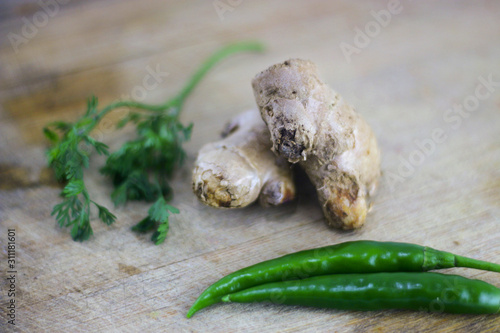 Fresh organic ginger with chilly and coriander leaves on wooden background.