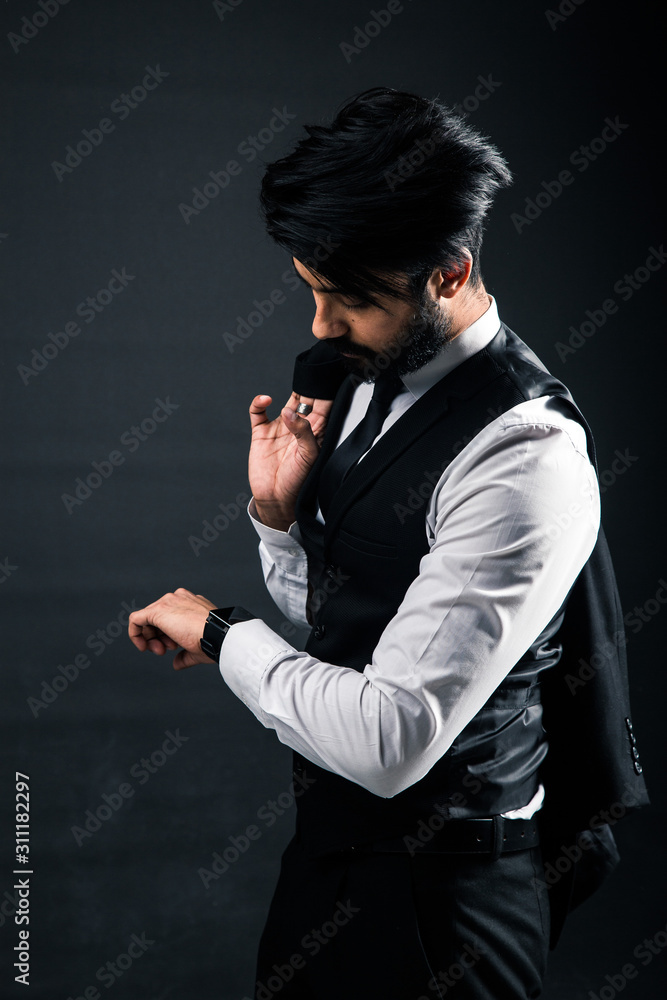 Portrait of a young handsome successful Indian in a classic black three-piece business suit on a dark background, Holding his jacket over his shoulder Portrait of a young handsome successful Indian in a classic black three-piece business suit on a dark background, Holding his jacket over his shoulder