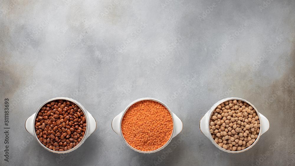 Fototapeta premium different types of legumes: red beans, red lentils, chickpeas. vegetarian food. banner, place for text. gray concrete background, top view