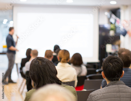 Seminar with expert speaker presenting to audience in hall. Blank business presentation screen for copy space. Executive presenter giving a speech. Leadership training coach in workshop lecture.