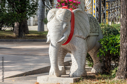 Beautiful white stone monument figure of an elephant with red ribbon is in a park in summer