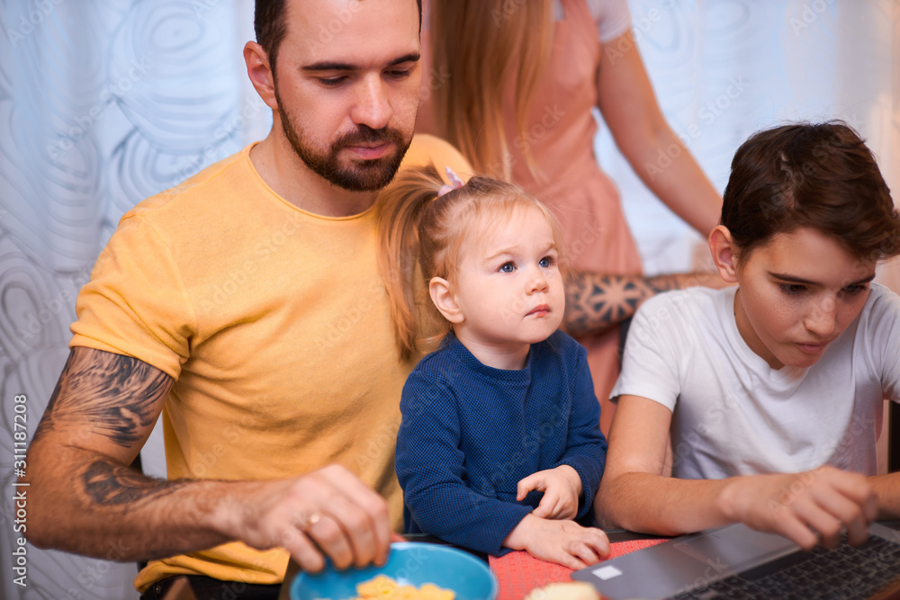 adorable kids and careful parents sit in kitchen with laptop, watching films and videos, eating fruits, having breakfast together at morning adorable kids and careful parents sit in kitchen with laptop, watching films and videos, eating fruits, having breakfast together at morning