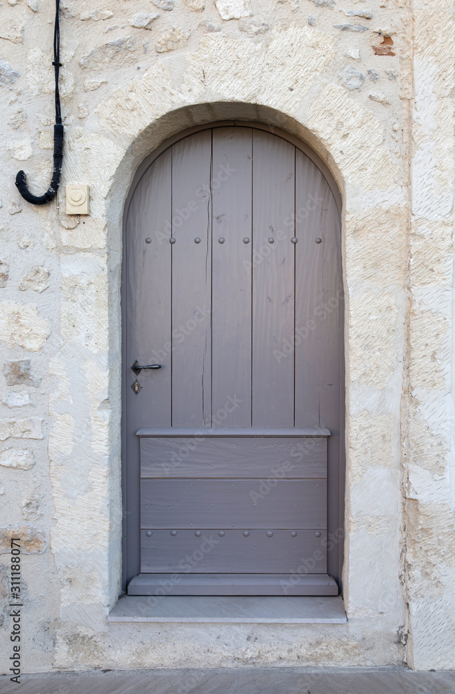 Old Grey door in an arched stone doorway with wooden panelling.