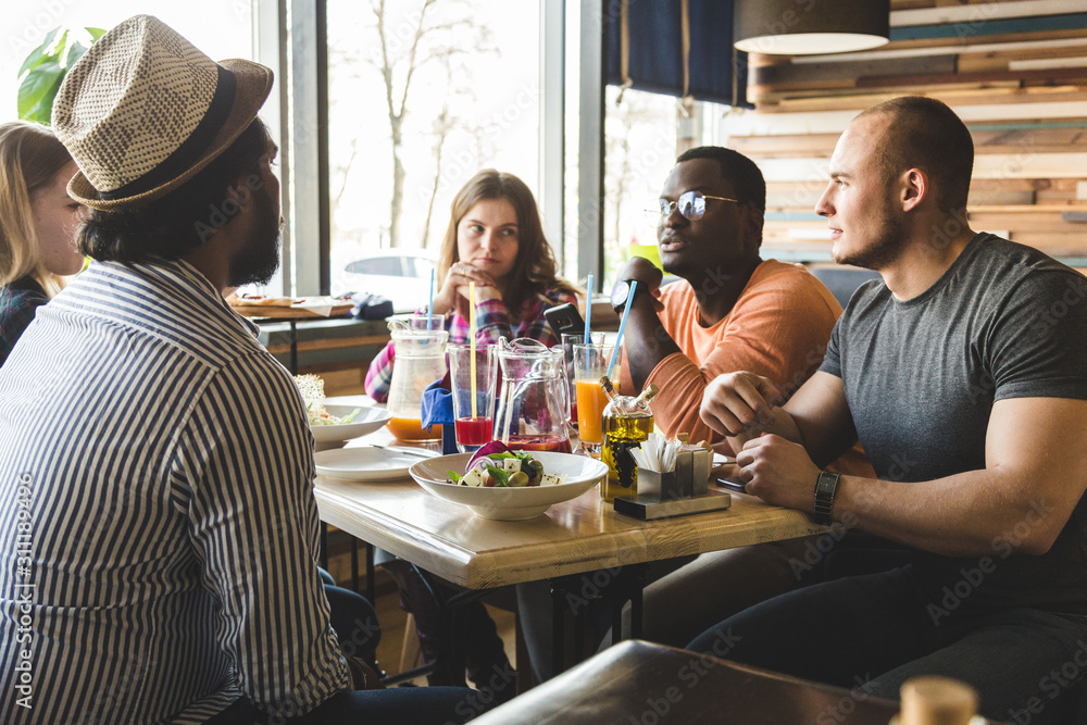 A company of multicultural young people in a cafe eating pizza, drinking cocktails, having fun A company of multicultural young people in a cafe eating pizza, drinking cocktails, having fun