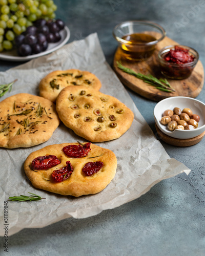 mini focaccia with olives, tomatoes, rosemary, pepper on parchment and gray background