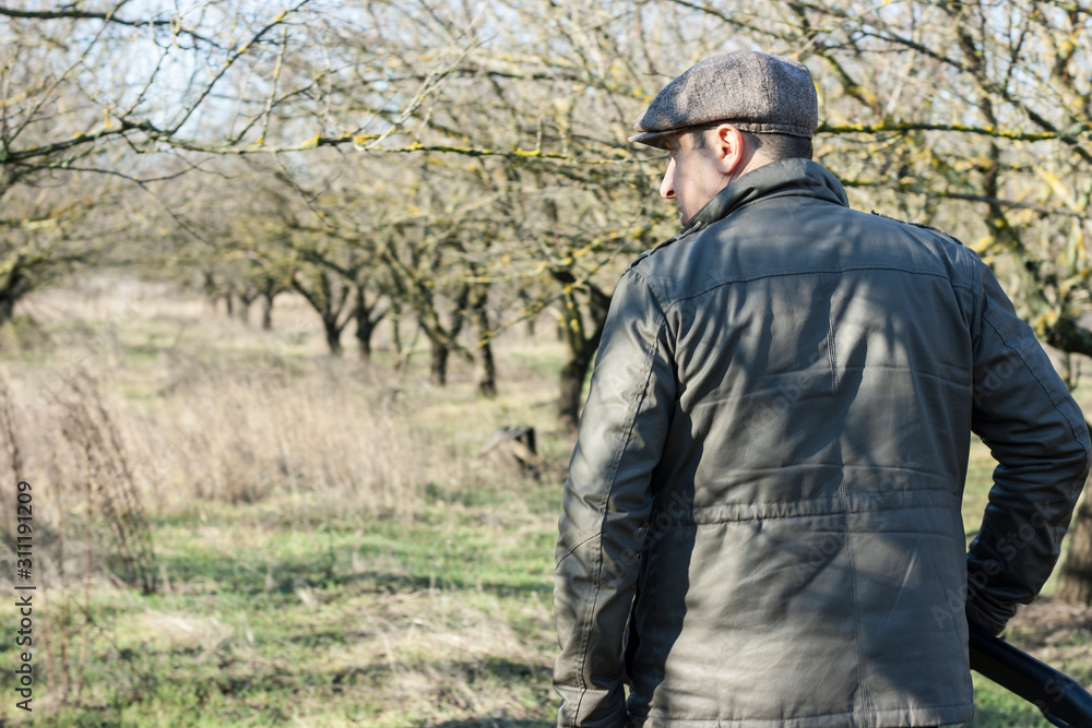A man with his back in a jacket and jeans with a hunting rifle in his hands is walking along the forest steppe in search of game A man with his back in a jacket and jeans with a hunting rifle in his hands is walking along the forest steppe in search of game