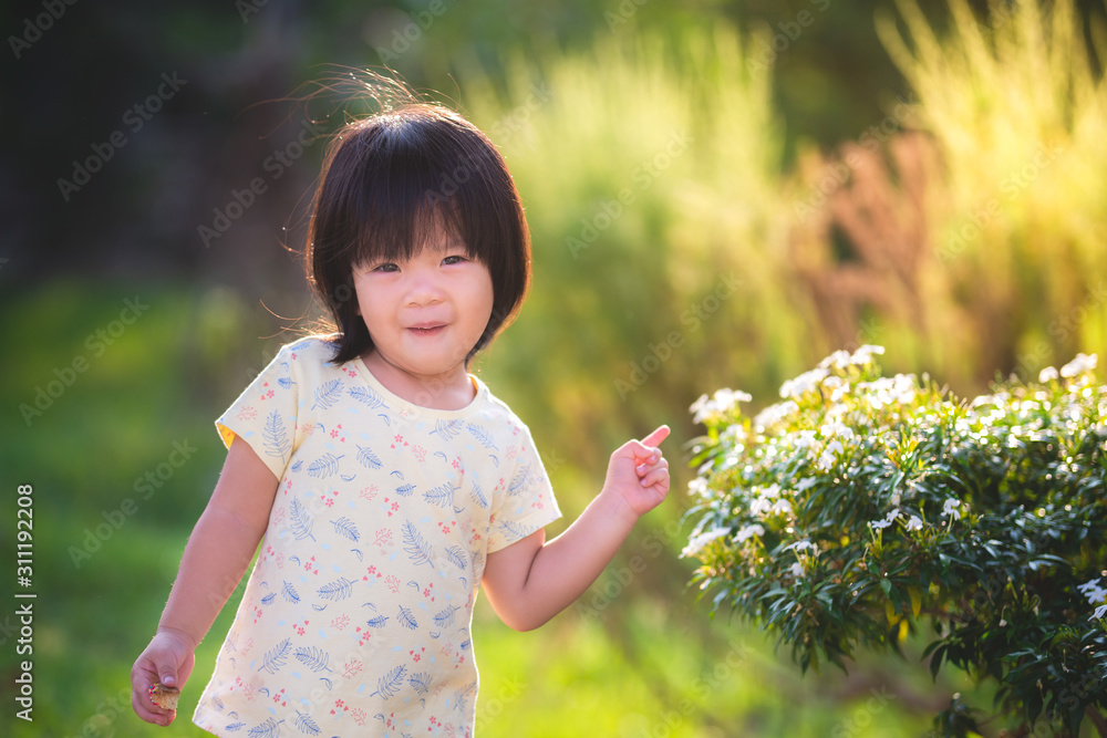 Adorable little child with spring or summer with beautiful background of green fields and golden shimmer. Cute girl raised his finger pointing, a small white flower. Baby age 2 years 9 months old. Adorable little child with spring or summer with beautiful background of green fields and golden shimmer. Cute girl raised his finger pointing, a small white flower. Baby age 2 years 9 months old.