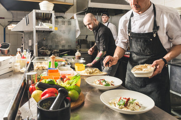 Professional chef cooking in the kitchen restaurant at the hotel, preparing dinner. A cook in an apron makes a salad of vegetables and pizza.