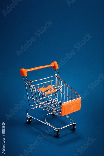 Empty shopping cart trolley on blue background with copy space