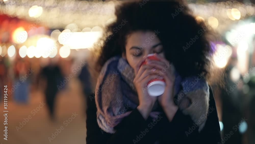 Close up portrait of happy afro american woman walking at the evening street and drinking hot coffee (or tea). Winter time. Handheld shot. Slowmotion. Close up portrait of happy afro american woman walking at the evening street and drinking hot coffee (or tea). Winter time. Handheld shot. Slowmotion.