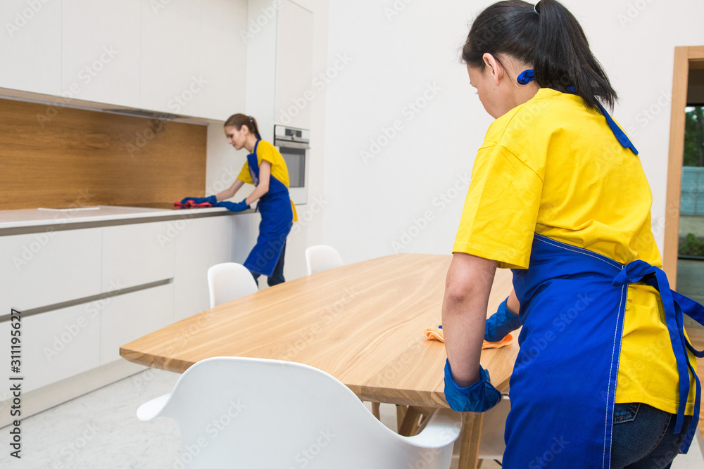 professional cleaning service. Two women in working uniform, in aprons, divide the cleaning of the kitchen of a private house, cottage. washing the refrigerator, tap, sink. Wash floor. professional cleaning service. Two women in working uniform, in aprons, divide the cleaning of the kitchen of a private house, cottage. washing the refrigerator, tap, sink. Wash floor.