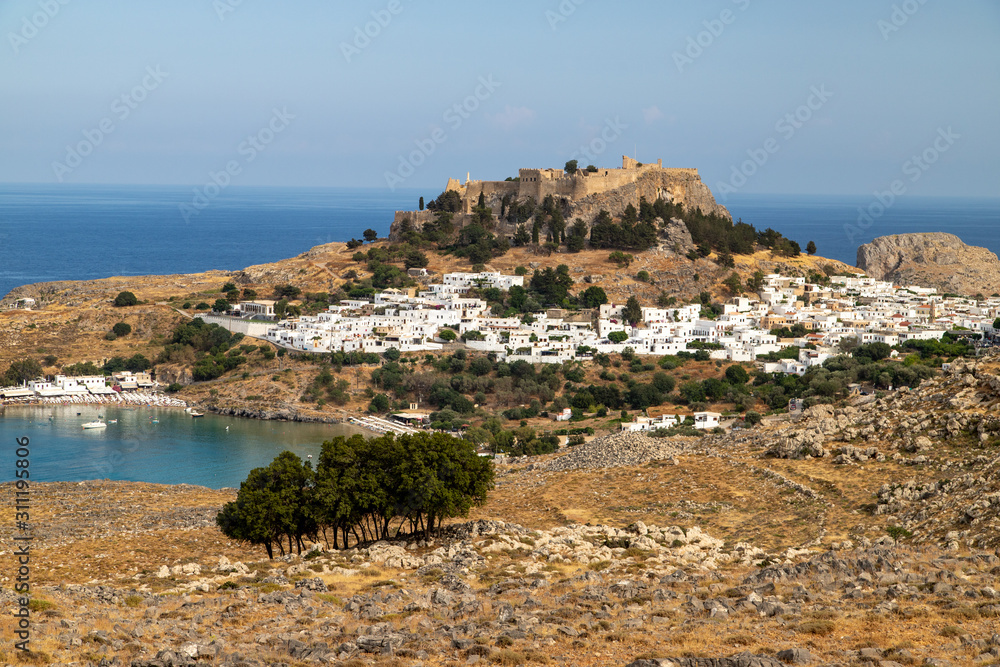 Scenic view at the city of Lindos with white houses, the antique Acropolis on top of the mountain and the bay