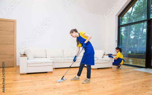 professional cleaning service. Two women in working uniform, in aprons, divide the cleaning of the kitchen of a private house, cottage. Washing floor