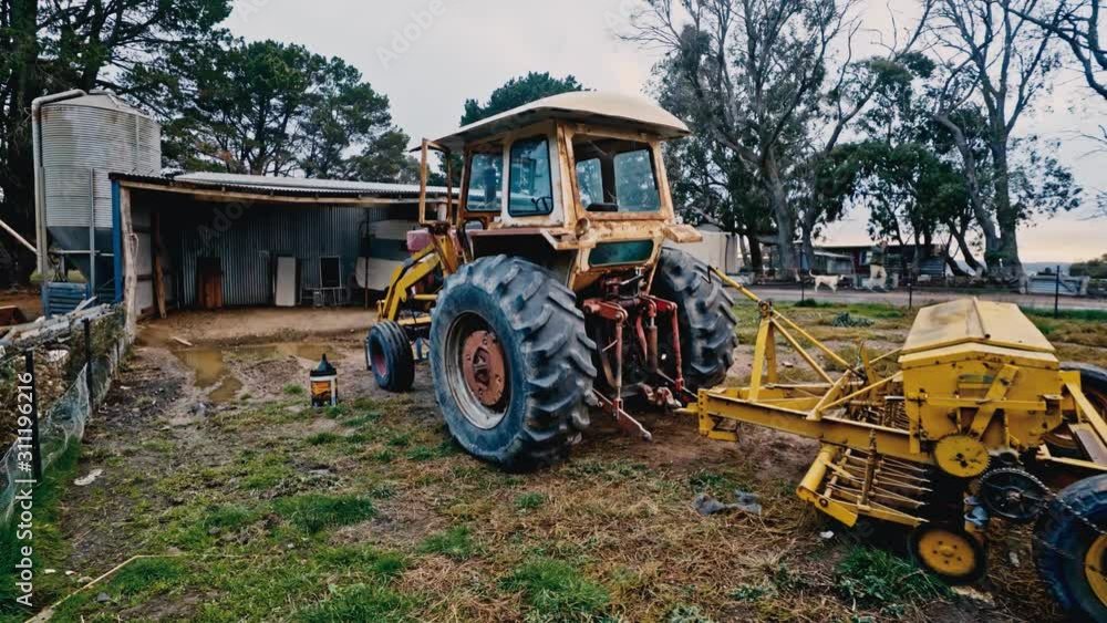 A rusty old tractor sits unused in a field as an Australian farmer starts off to work in the distance A rusty old tractor sits unused in a field as an Australian farmer starts off to work in the distance