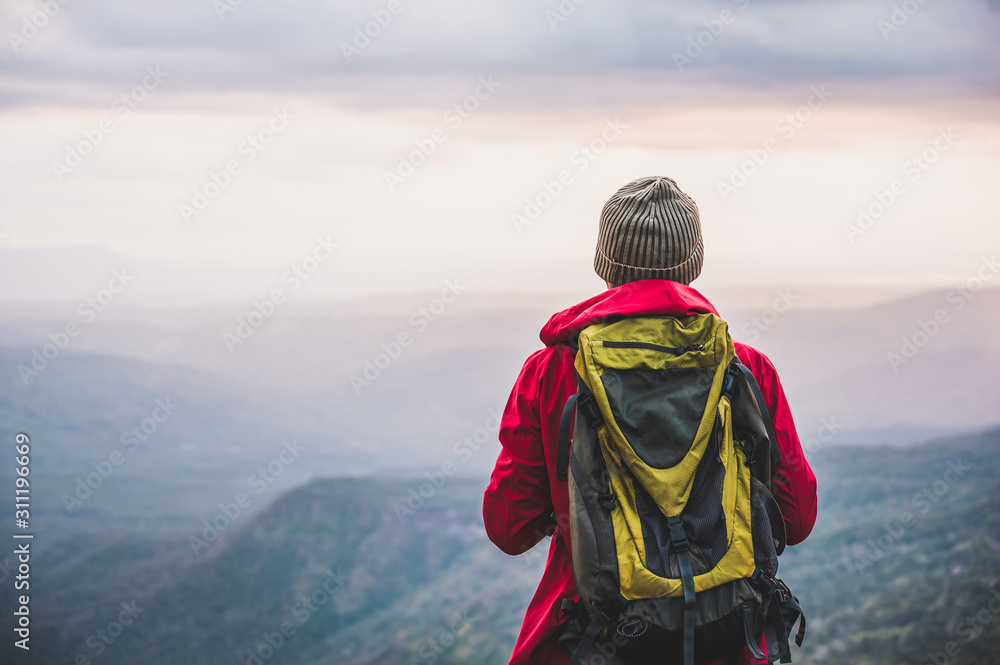 Hikers climbing a red rain jacket carrying a backpack Standing on the edge of a cliff See the beauty of the mountains at sunset, showing success, freedom and adventure.