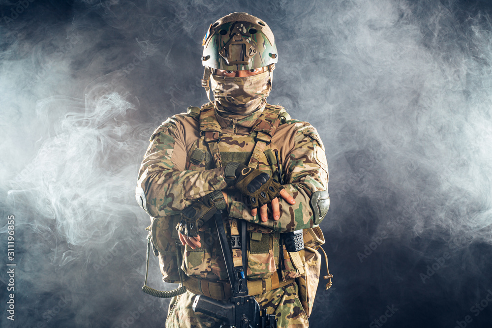 young military man confidently looking at camera in smoky space, wearing green uniform for soldiers and helmet young military man confidently looking at camera in smoky space, wearing green uniform for soldiers and helmet