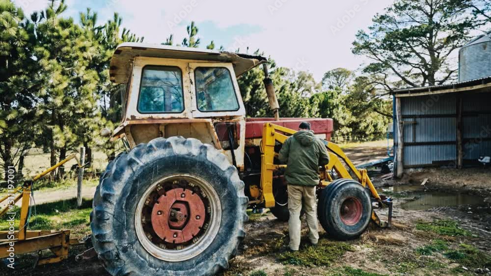 An Australian farmer works on his old and rusted tractor with some lubricant. Dolly in An Australian farmer works on his old and rusted tractor with some lubricant. Dolly in