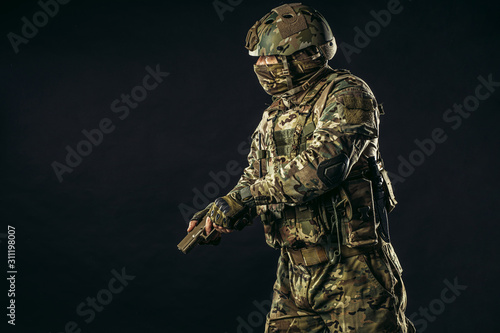 fearless brave strong man with gun isolated in black space, in readiness to shoot at enemy, wearing military uniform