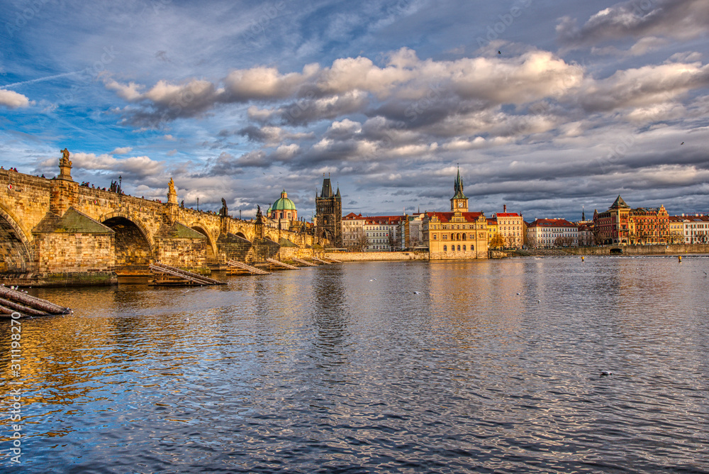 Naklejka premium Beautifully illuminated Charles Bridge at sunset with surrounding buildings, Prague