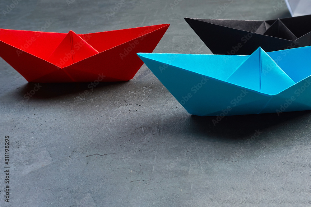 Business leadership Concept, Paper Boat, the key opinion Leader, the concept of influence.Red.blue and black paper boat as the Leader on a gray concrete background