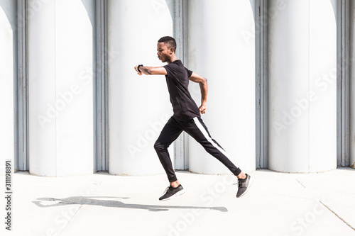 Fototapeta Naklejka Na Ścianę i Meble -  Athletic young afroamerican man running on the promenade. Black Male runner sprinting outdoors. Healthy lifestyle concept.