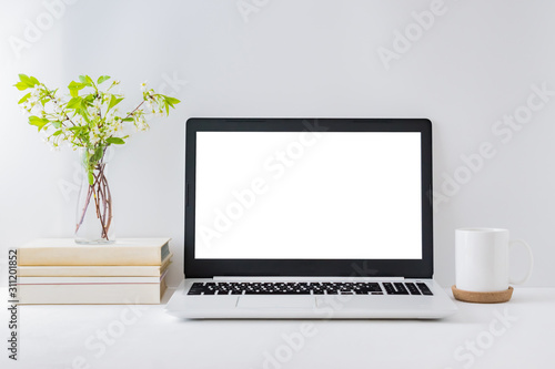 Office workspace with laptop mockup, books, spring flowers in a vase, office supplies on a light background