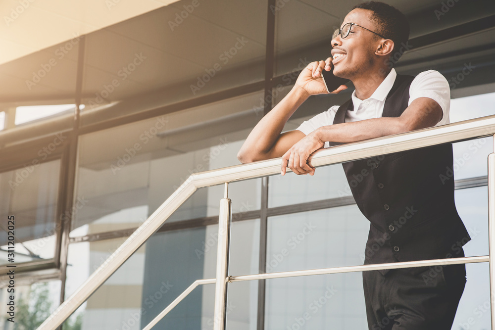 Young african american business man in suit and eyeglasses talking on the phone on the background of the business center Young african american business man in suit and eyeglasses talking on the phone on the background of the business center