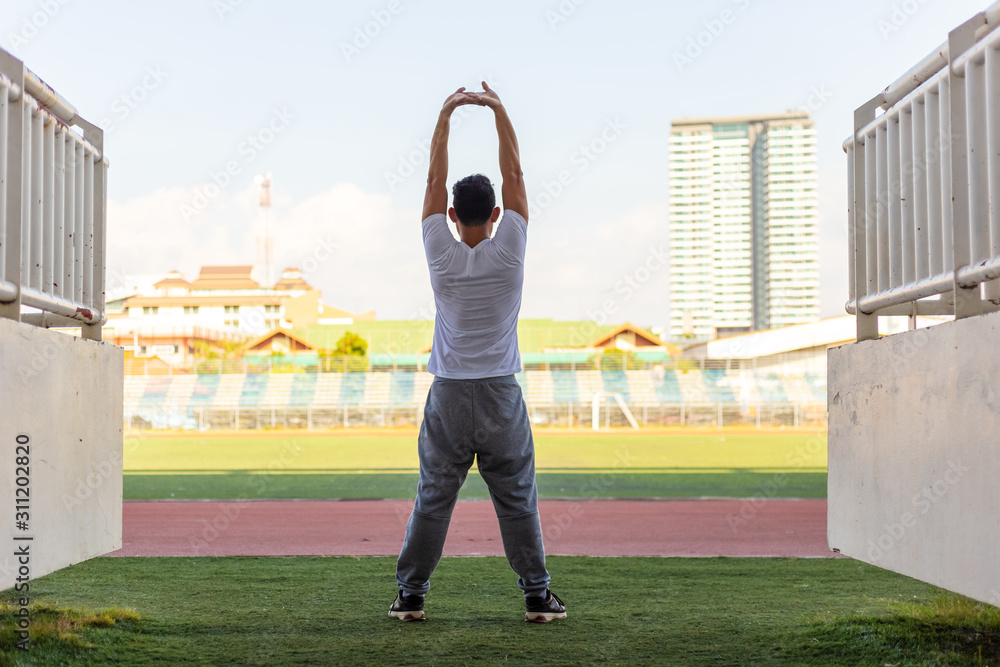 Full length portrait of a athletic man stretching in the morning and standing at sport stadium.