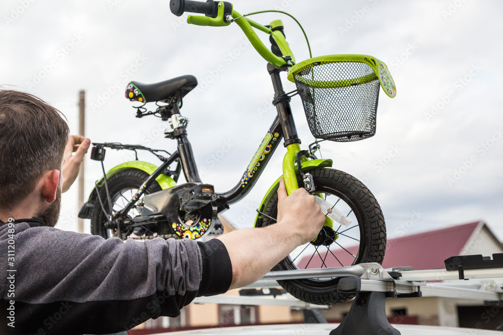 Bicycle transportation - A man fastens and installs a children's bicycle on the roof of a car in a special mount for bicycle transport. The decision to transport large loads and travel by car. Bicycle transportation - A man fastens and installs a children's bicycle on the roof of a car in a special mount for bicycle transport. The decision to transport large loads and travel by car.