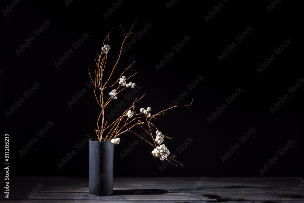 Branch of a bush of a snowberry in a vase on a dark background. Ikebana.
