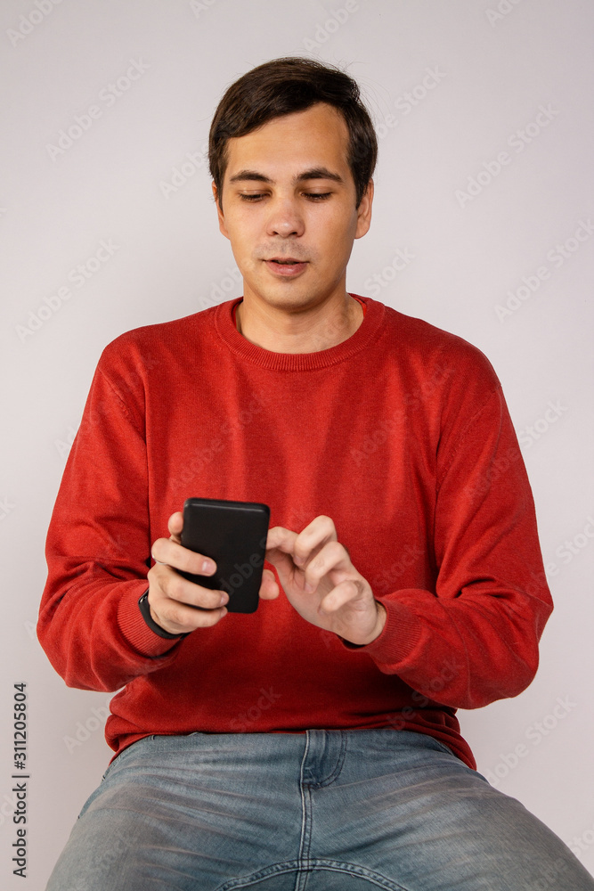 The guy in the red sweater is using a smartphone. Examines the image The guy in the red sweater is using a smartphone. Examines the image
