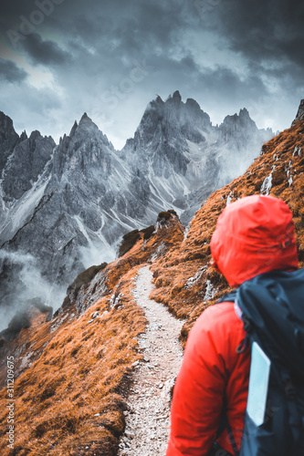 Back view of a hiker trekking and contemplating dramatic panorama. Travel and adventure with a traveler with backpack looking at amazing mountains, wanderlust travel concept, moody epic moment