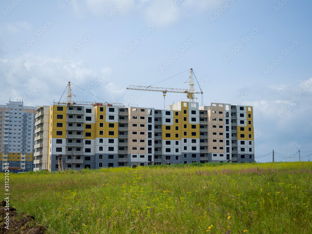 Tower cranes build a multi-storey building from colored panels. Summer sunny day Tower cranes build a multi-storey building from colored panels. Summer sunny day