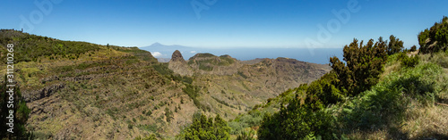 Panoramic view of Tenerife Island with volcano Teide above horizon and Los Roques peaks near Garajonay national park at La Gomera. Thickets of relic laurels and heather on steep green slopes. Canary