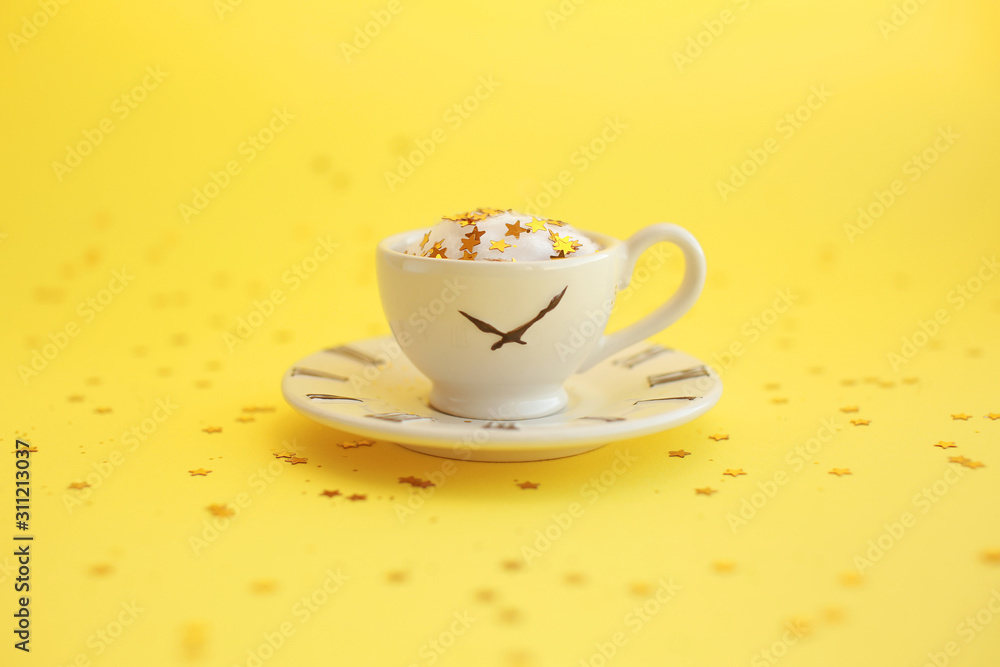 Fototapeta premium Ceramic white cup with glitter stars inside and small saucer with clock face icon. Yellow background.
