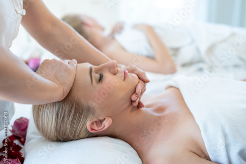 Foreign women are happy and relaxed with a Thai massage on the head by a professional Thai masseuse while lying on the bed. Facial massage is one of the world famous relaxation