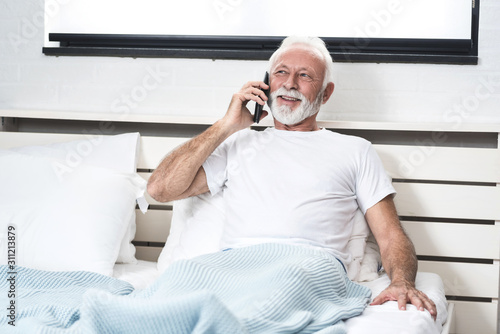 Senior man using mobile phone in bed in his room photo