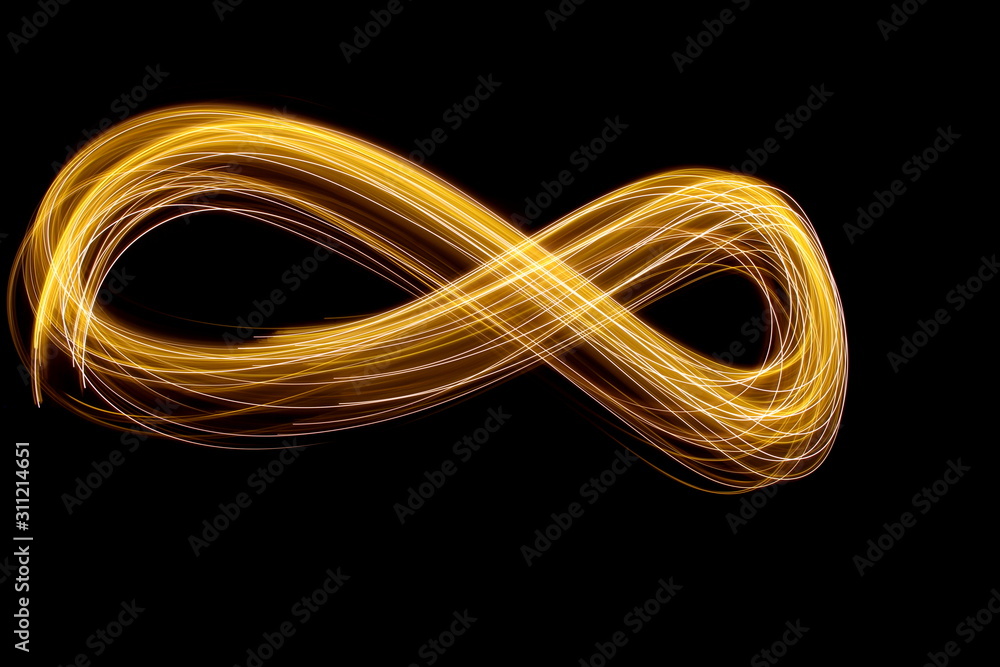 Long exposure photograph of an infinity loop in gold neon colour in an abstract swirl, parallel lines pattern against a black background. Light painting photography. Long exposure photograph of an infinity loop in gold neon colour in an abstract swirl, parallel lines pattern against a black background. Light painting photography.
